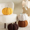 A yellow pumpkin plush decoration sits on a white chair next to a dark brown pumpkin on a light gray surface.