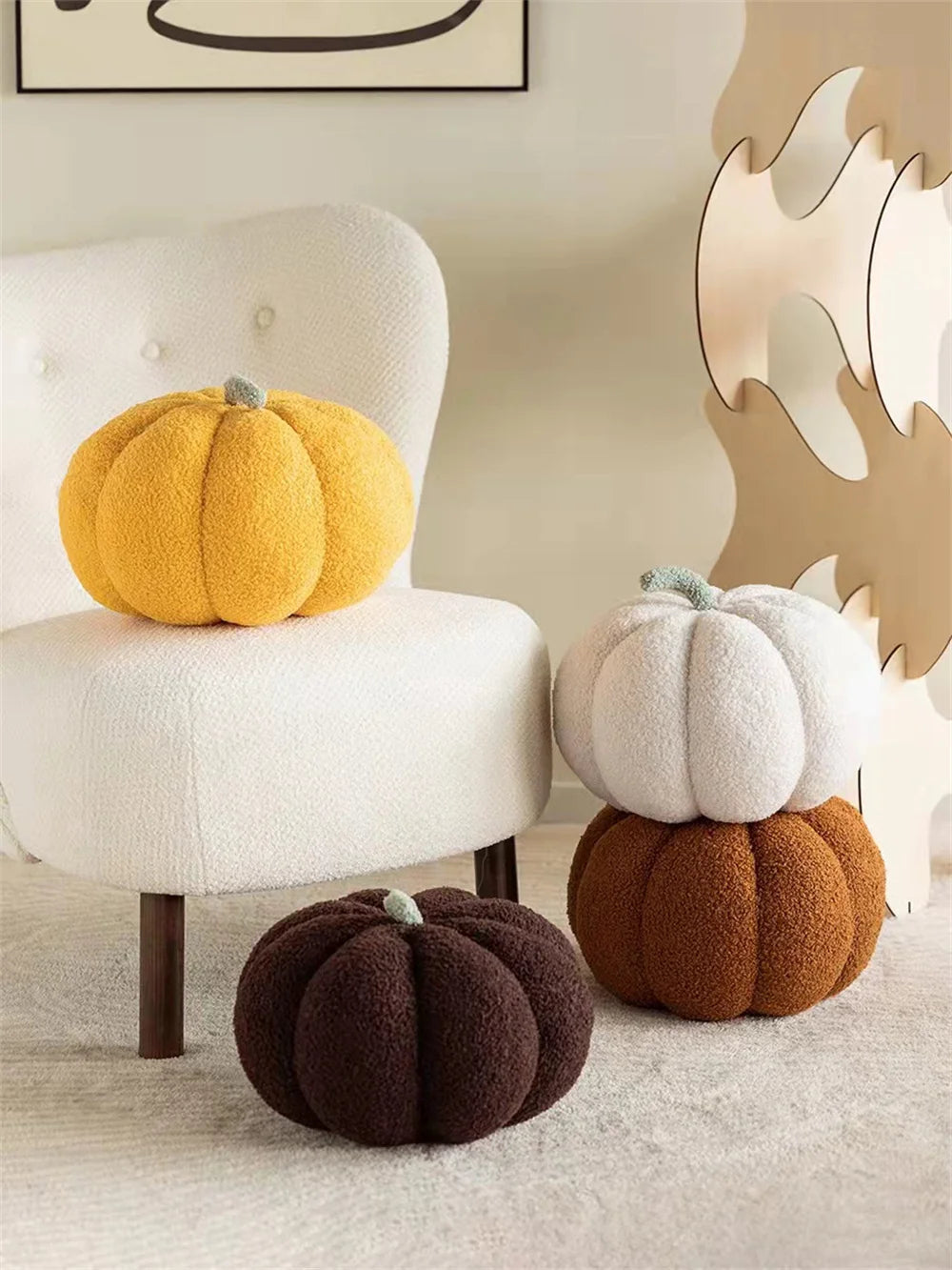 A yellow pumpkin plush decoration sits on a white chair next to a dark brown pumpkin on a light gray surface.