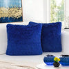A set of two deep blue faux fur throw pillows resting on a white sofa near a window.