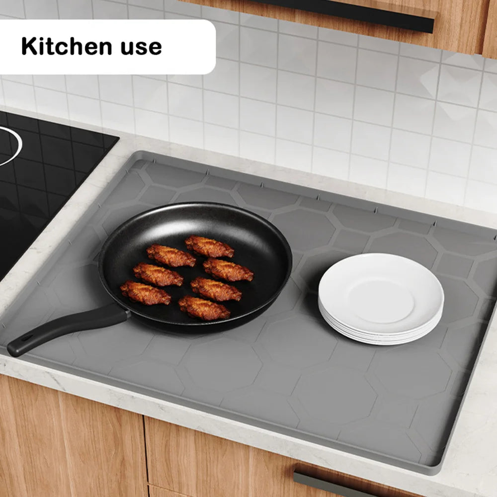 A silicone mat used for kitchen use placed on a countertop, featuring a frying pan and plates.