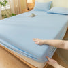 A light blue fitted bed sheet is draped over a bed, with a hand touching the fabric.