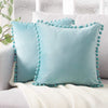 A light blue velvet decorative cushion cover with a textured trim resting on a white knitted blanket.
