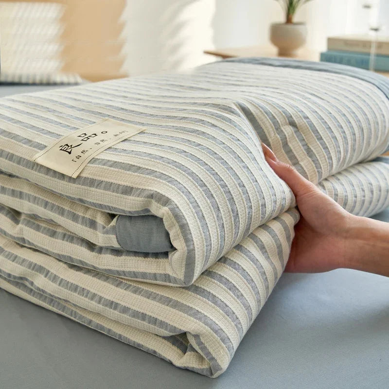 A close-up of a striped light gray luxury jacquard summer quilt being held by a hand.