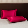 A vibrant magenta satin pillow and fitted sheet resting on a beige bed with a dark brown headboard.