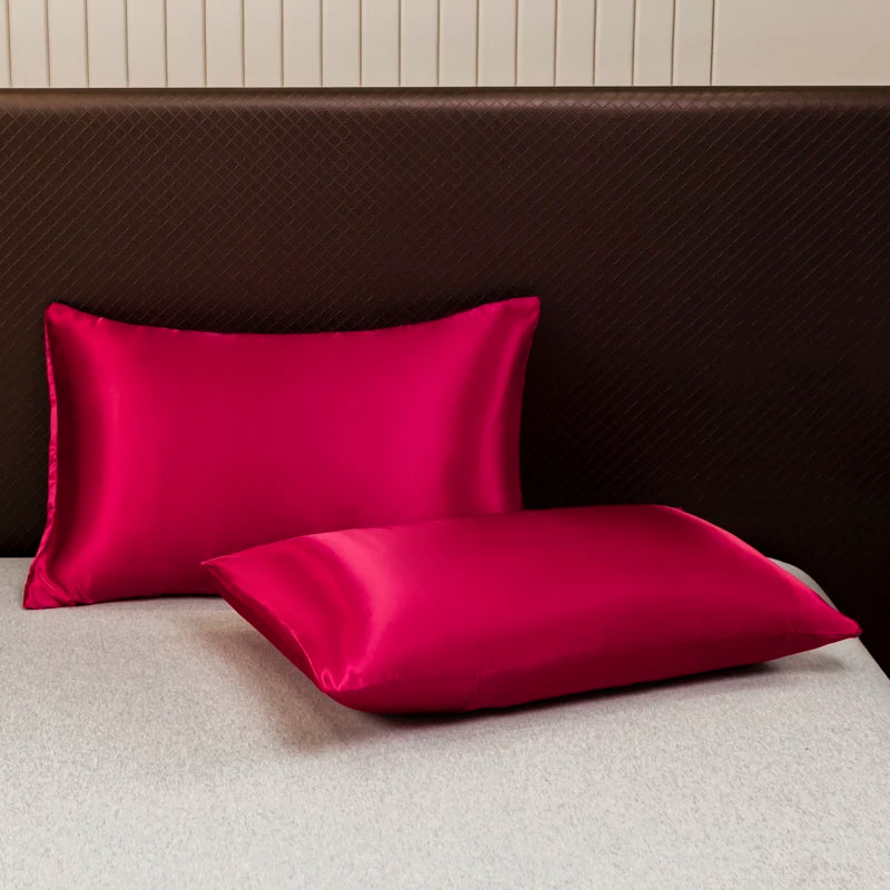 A vibrant magenta satin pillow and fitted sheet resting on a beige bed with a dark brown headboard.