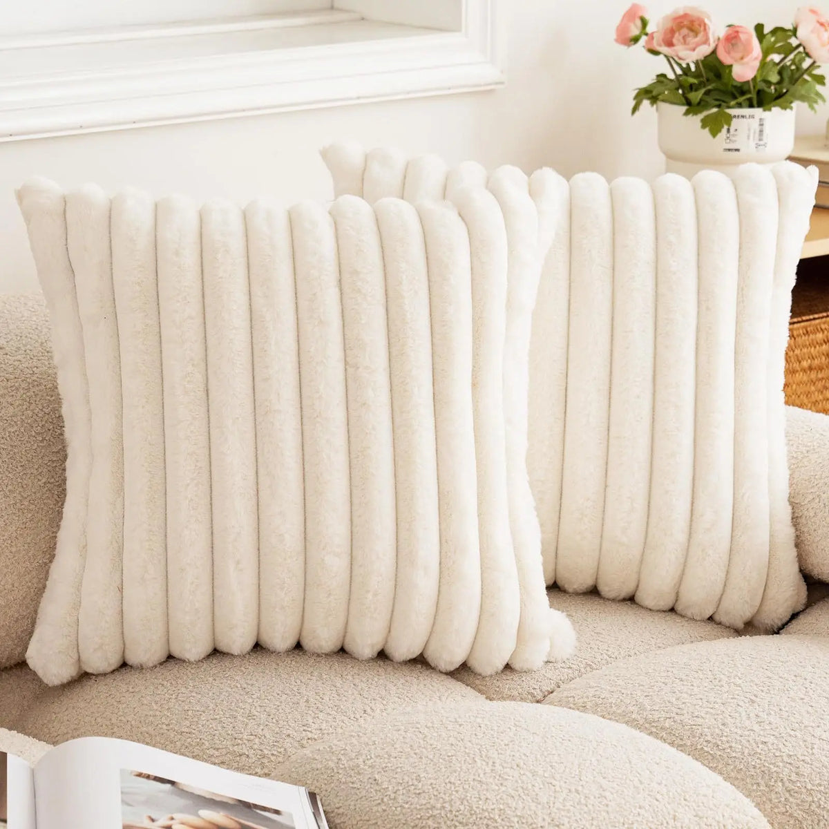 A close-up of a cream colored square faux rabbit fur cushion cover resting on a beige sofa.