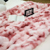 A pink faux rabbit fur throw blanket draped on a white surface with a numbered card resting on the fabric.