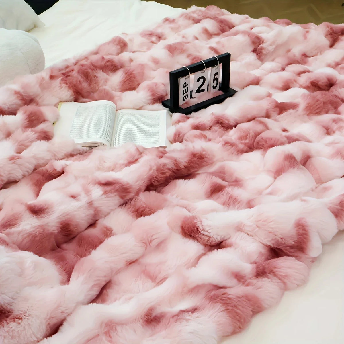 A pink faux rabbit fur throw blanket draped on a white surface with a numbered card resting on the fabric.