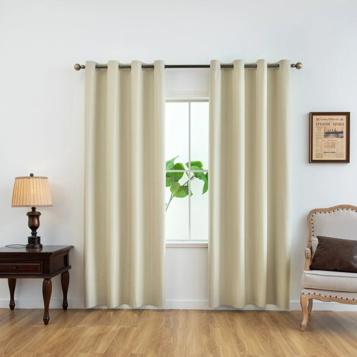 Cream-colored blackout window curtains hanging in a window frame with a wooden table and chair nearby.