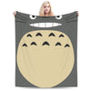 A person is holding up a fleece throw blanket featuring a large, smiling Totoro character face.