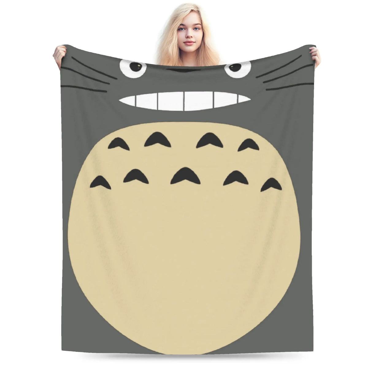 A person is holding up a fleece throw blanket featuring a large, smiling Totoro character face.