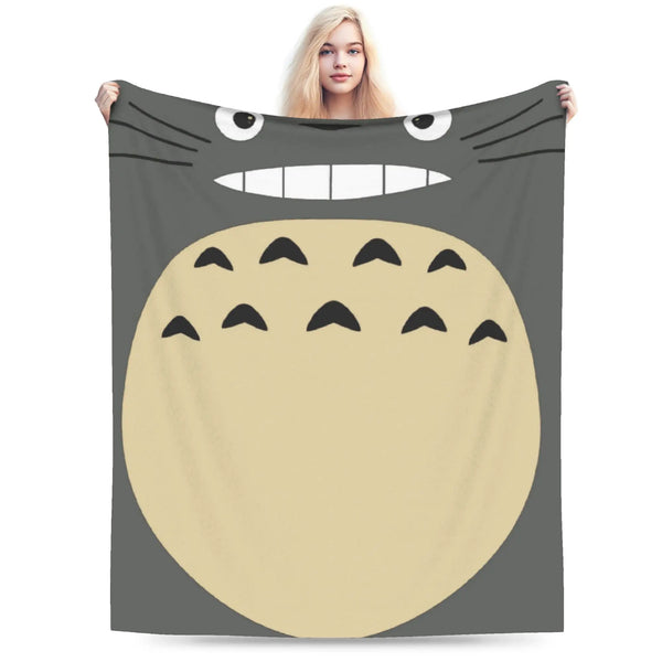 A person is holding up a fleece throw blanket featuring a large, smiling Totoro character face.