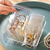 A hand is holding a clear plastic storage box filled with small jewelry bags for dustproof self-sealing storage.