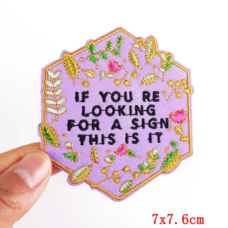 A purple embroidered patch shaped like a flower with green and pink leaves, featuring the text If you are looking for a sign 