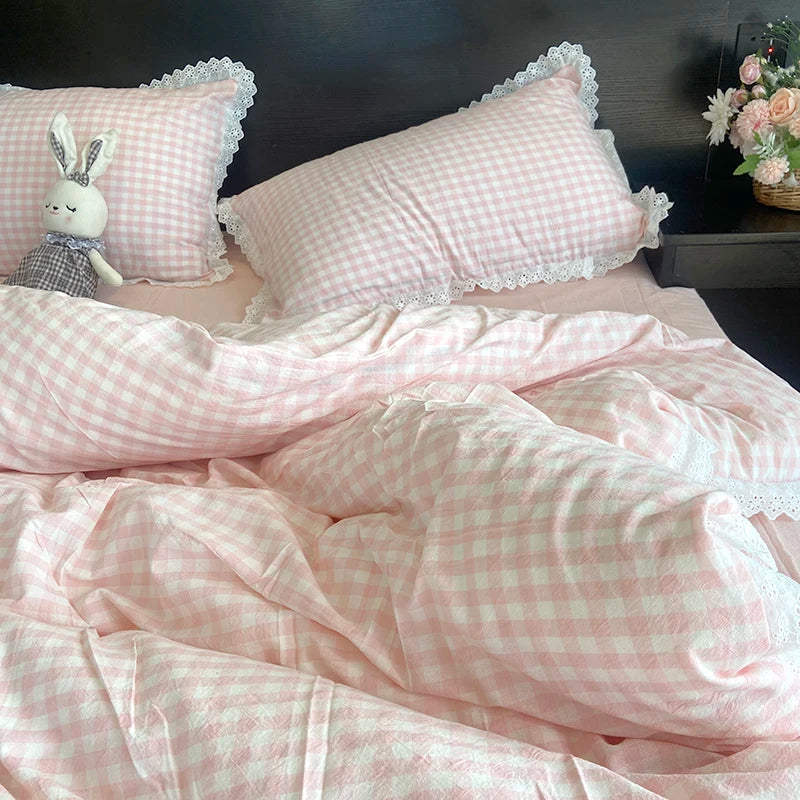 A pink gingham duvet cover and pillowcase set with white lace trim, featuring a decorative bunny plush toy.