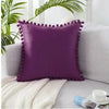 A deep purple velvet decorative cushion cover resting on a light gray sofa with a white knitted throw.