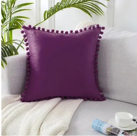 A deep purple velvet decorative cushion cover resting on a light gray sofa with a white knitted throw.