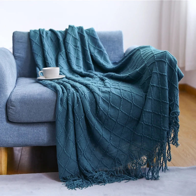 A teal knitted tassel throw blanket draped over a gray sofa.