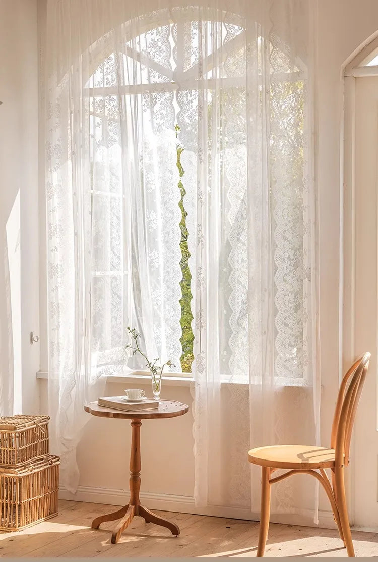 A sheer white floral lace curtain hangs in a large arched window, letting natural light illuminate the room.