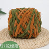 A ball of olive green and orange chenille knitting yarn resting on a woven straw mat.