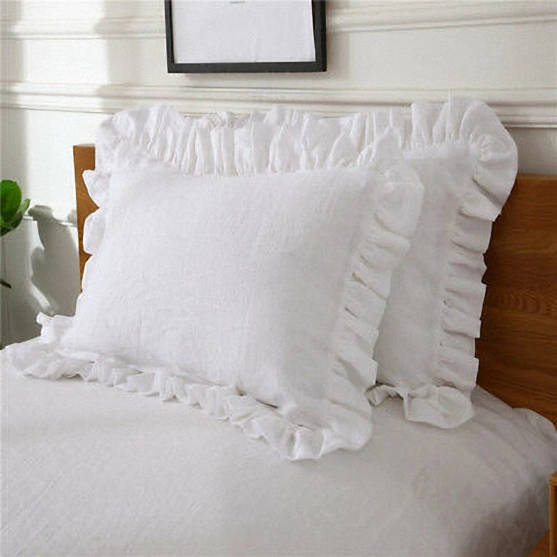 White soft cotton ruffle pillow cover resting on a bed with a wooden headboard.