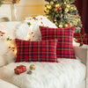 Two red and green tartan plaid decorative throw pillow covers resting on a white faux fur surface near a decorated Christmas 