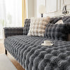 A dark gray plush rabbit fur sofa cushion cover draped over a sofa, with a light colored cushion resting on top.