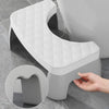 A white adjustable adult toilet squat stool with a diamond-patterned seat is shown next to a hand for scale.