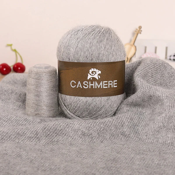 A ball of gray cashmere yarn with a brown label and a skein of yarn resting on a gray knitted fabric.