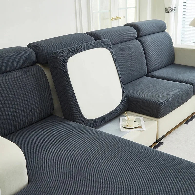 A dark gray jacquard elastic sofa cushion slipcover with a white accent cushion on a light-colored sofa.