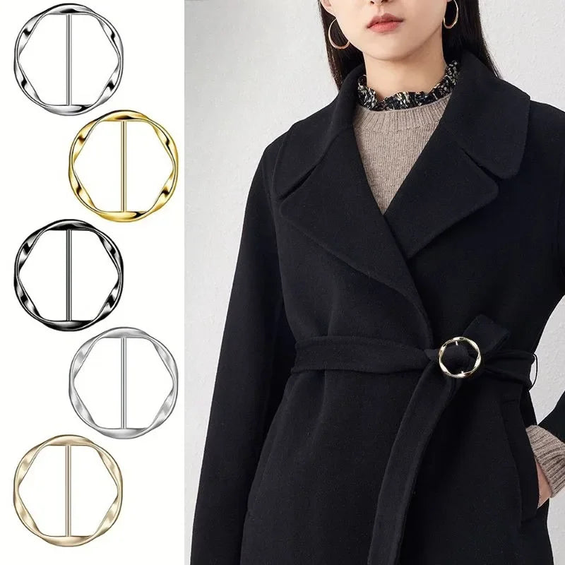 A woman models a black coat featuring a metal round clip buckle detail on the fabric.