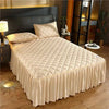 A beige embroidered quilted bed skirt covering a queen mattress in a bedroom setting.