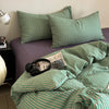 A close-up of a striped duvet cover set in shades of green and purple on a bed.