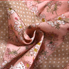 Pink floral patterned fabric for a kitchen apron featuring a dotted beige background and white flowers.