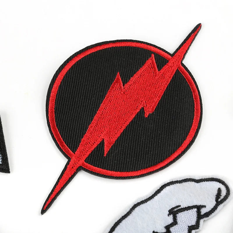 A black circular embroidered patch featuring a red lightning bolt design on a white background.