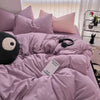 A soft lavender duvet cover set with matching pillows and a black eye mask are displayed on a bed.