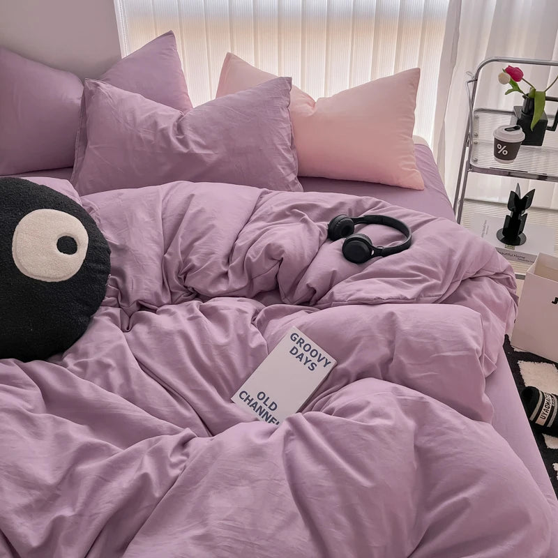 A soft lavender duvet cover set with matching pillows and a black eye mask are displayed on a bed.