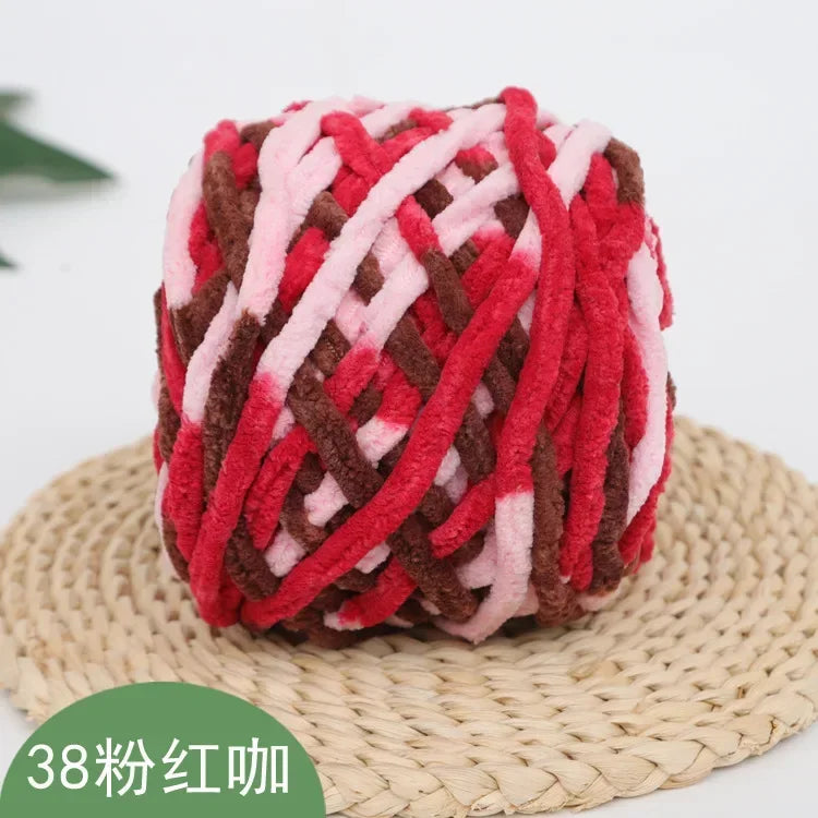 A ball of red and pink chenille knitting yarn resting on a woven straw mat.