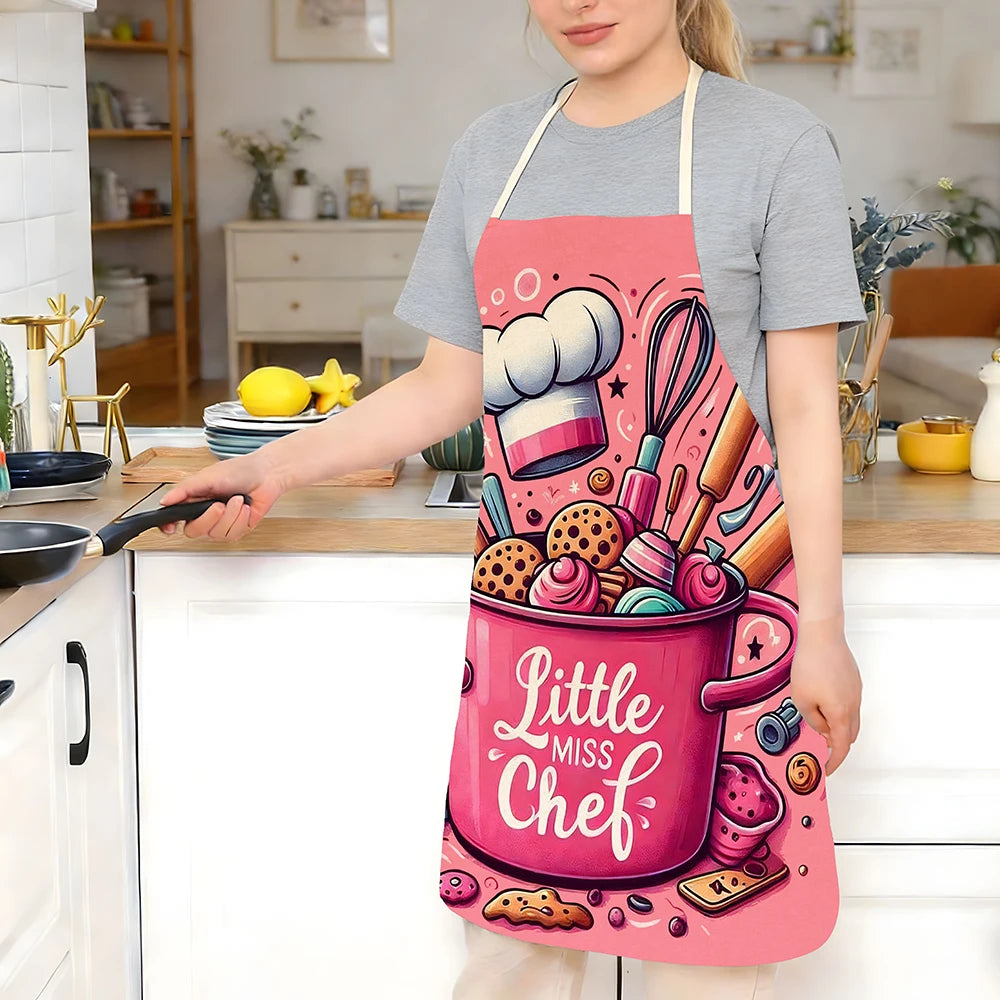 A woman wearing a pink kitchen apron with baking designs is standing at a kitchen counter.
