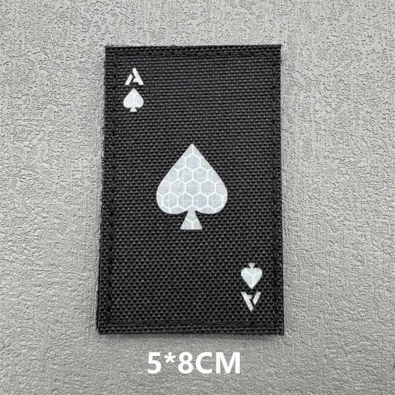 A black tactical patch featuring a white spade symbol on a gray background.