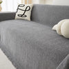 A gray chenille sofa cover with a white embroidered pillow and light-colored decorative pillows.