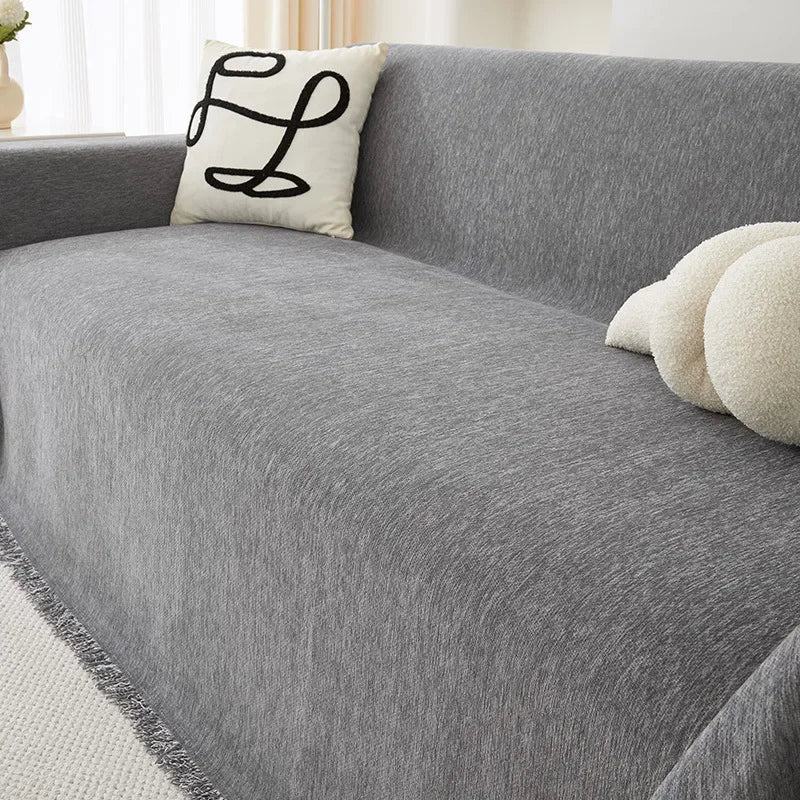 A gray chenille sofa cover with a white embroidered pillow and light-colored decorative pillows.