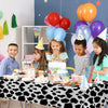 A table set for a birthday party featuring a cow print disposable plastic tablecloth and colorful balloons