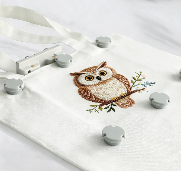 A white fabric bag with several magnetic embroidery hoops featuring an owl design.