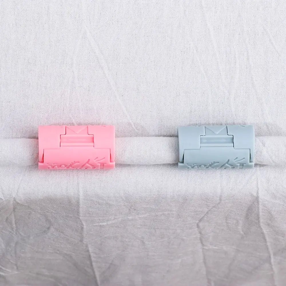 Two plastic invisible sheet clips, one pink and one light blue, are shown against a white fabric background.