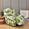 A white slipcover recliner features a vibrant green tropical leaf print on a wooden floor.