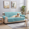 A light teal reversible sofa slipcover on a beige frame is displayed in a modern living room setting.