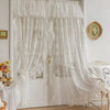 A sheer white curtain with ruffled lace trim and vintage floral design hanging in a bright room.