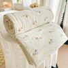 A cream-colored quilt blanket with a pastoral print featuring small animals and flowers, rolled up on a white surface.