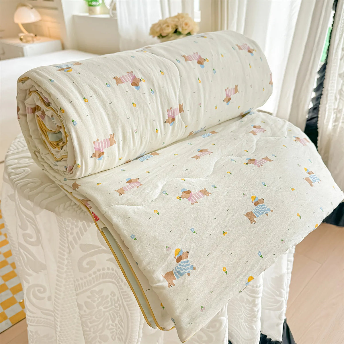 A cream-colored quilt blanket with a pastoral print featuring small animals and flowers, rolled up on a white surface.